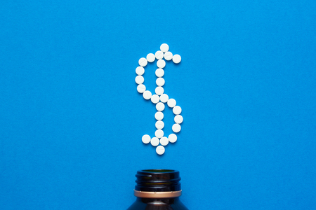 white pills in the shape of a dollar are scattered on a blue background next to a dark bottle. Top viewの写真素材