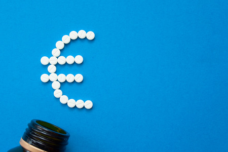 white pills in the shape of a euro are scattered on a blue background next to a dark bottle.の写真素材