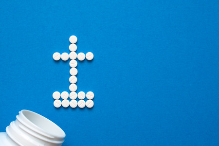 white pills in the shape of a grave cross are scattered on a blue background next to a white bottle. Depression, harm of drugs concepts. Top view with copyspaceの写真素材