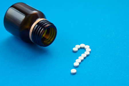 white pills in the shape of a question mark are scattered on a blue background next to a dark bottle.の写真素材