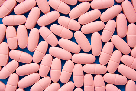 A lot of pink pills on blue background texture close up.の写真素材