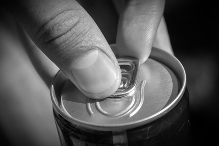 Man's hands opening can of beer close up at sunny day. Fresh drink at warm day. Alcohol drink. Alcohol addiction concept with black and white effectの写真素材