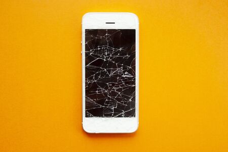 Broken screen of smartphone on the orange background. Smashed glass of cell phone, illustration for repair, fix phone services. Top viewの写真素材