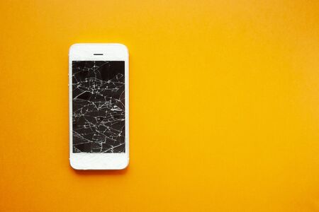 Broken screen of smartphone on the orange background. Smashed glass of cell phone, illustration for repair, fix phone services. Top view with copyspaceの写真素材