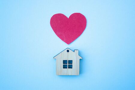 Love home, insurance and mortgage, marriage and valentine concept. Small wooden house toy and paper heart shape on blue background top view の写真素材