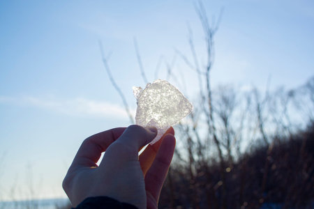Piece of ice in man's hand close up against the sun. Look at the sun through the iceの写真素材