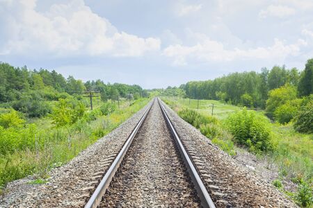 A railway through the summer green fields.  Beautiful green railway tree landscape sky clouds. Beautiful landscape. Railway transport. の写真素材