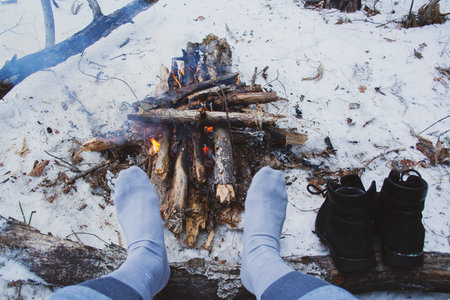 Man's legs against the bonfire in the forest. Bushcraft symbol. Solo survival in nature. Winter in...