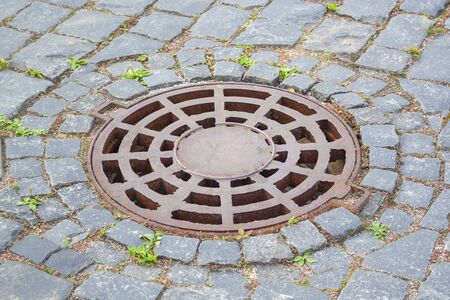 Manhole cover near paving stones. Rusty manhole cover on the walkside with paving stonesの写真素材