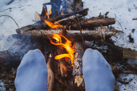 Man's legs against the bonfire in the forest. Bushcraft symbol. Solo survival in nature. Winter in...