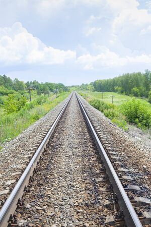 A railway through the summer green fields.  Beautiful green railway tree landscape sky. Beautiful landscape and railway. Railway transport. Verticalの写真素材