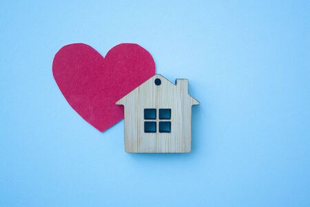 Love home, insurance and mortgage, marriage and valentine concept. Small wooden house toy and paper heart shape on blue background top view の写真素材