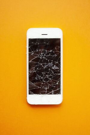 Broken screen of smartphone on the orange background. Smashed glass of cell phone, illustration for repair, fix phone services. Top view verticalの写真素材
