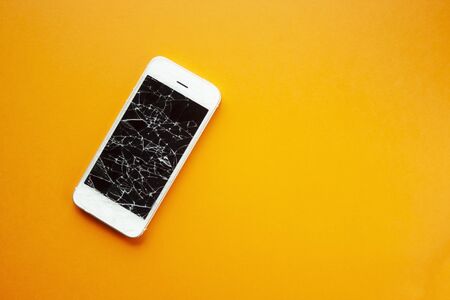 Broken screen of smartphone on the orange background. Smashed glass of cell phone, illustration for repair, fix phone services. Top view with copyspaceの写真素材