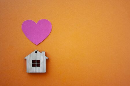 Love home, insurance and mortgage, marriage and valentine concept. Small wooden house toy and paper heart shape on orange background top view copyspaceの写真素材