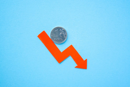 one rouble coin on blue background with red arrow down. exchange rate chart. ruble depreciation....