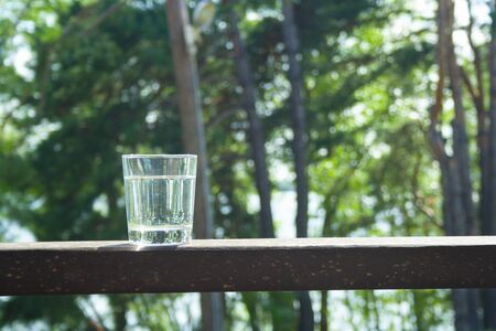 Water glass stands on wooden plank on sunbeams. Hydration, hot summer days concept. Healthy lifestyle symbol. Healthy water drink with copy space の写真素材
