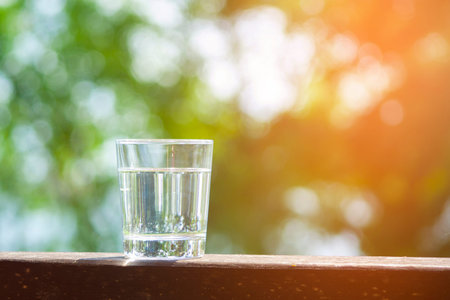 Water glass stands on wooden plank on sunbeams. Hydration at hot summer days concept. Healthy...
