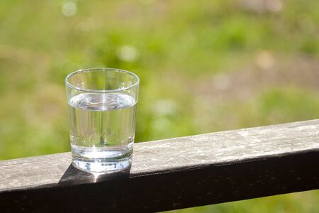Water glass stands on wooden plank on sunbeams. Hydration at hot summer days concept. Healthy lifestyle symbol. Healthy water drinkの写真素材