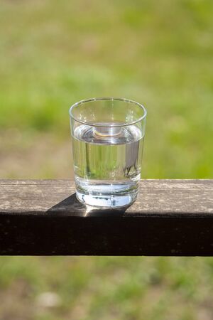 Water glass stands on wooden plank on sunbeams. Hydration at hot summer days concept. Healthy lifestyle symbol. Healthy water drink verticalの写真素材