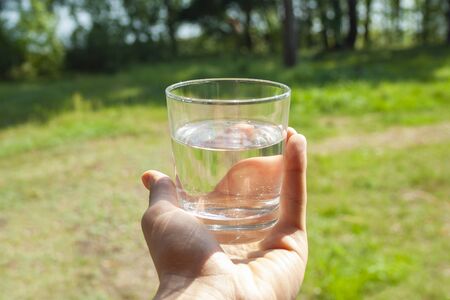 Water glass at man's hand on sunbeams. Hydration at hot summer days concept. Healthy lifestyle symbol. Healthy water drink toned verticalの写真素材