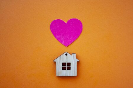 Love home, insurance and mortgage, marriage and valentine concept. Small wooden house toy and paper heart shape on orange background top view の写真素材