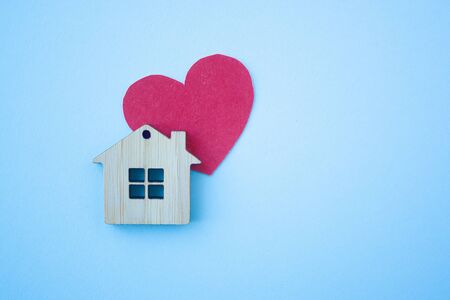 Love home, insurance and mortgage, marriage and valentine concept. Small wooden house toy and paper heart shape on blue background top view copyspaceの写真素材