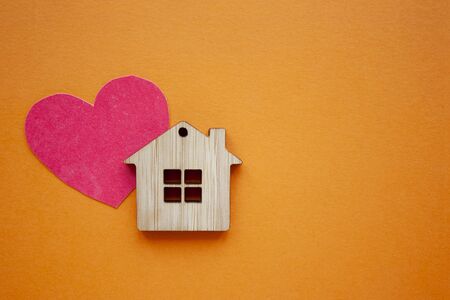 Love home, insurance and mortgage, marriage and valentine concept. Small wooden house toy and paper heart shape on orange background top view copyspaceの写真素材