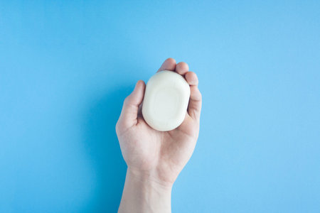 A piece of soap in a male hand a top view on a blue background. The human hand holds soap. Wash your...