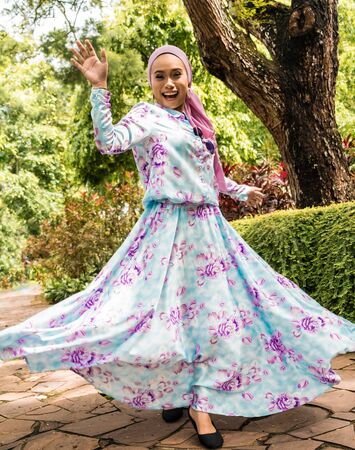 Beautiful woman in a long blue dress with purple flowers twirls in a parkの写真素材