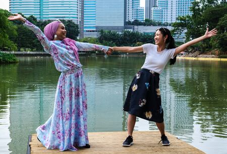 A malay and chinese girl stretch out their arms in celebration of their friendshipの写真素材