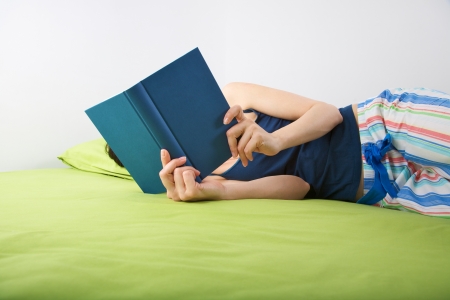 woman lying on a green bed reading a bookの写真素材