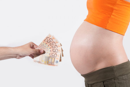offering Euro banknotes to tummy of naked pregnant womanの写真素材