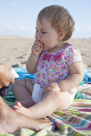 portrait of one year baby eating banana on towel next to mom at beachの写真素材