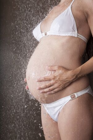 pregnant woman with white bikini under shower waterの写真素材