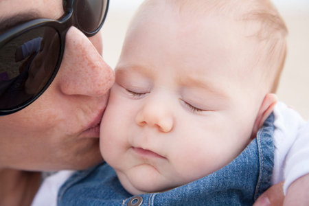 woman black sunglasses kissing three month baby with jeans dress