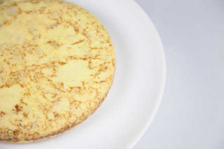 white dish with yellow spanish potato omelette on grey tablecloth