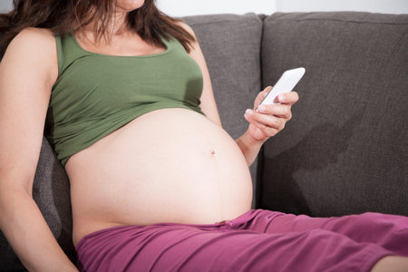 pregnant woman reading smartphone sitting in sofa