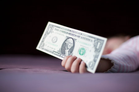 closeup one dollar banknote in hand of blonde caucasian baby nineteen month age with pink and white...