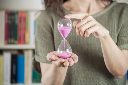 pink sand clock in woman hands over library backgroundの写真素材
