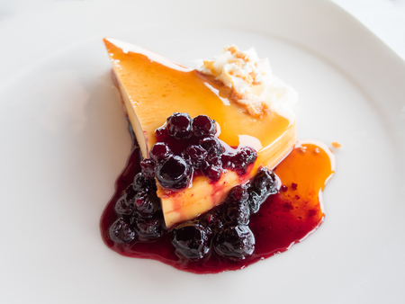 piece of cheese cake orange jam with strawberry jam with red fruits berries almond chopped and whipped cream on white modern dish over white tablecloth restaurantの写真素材