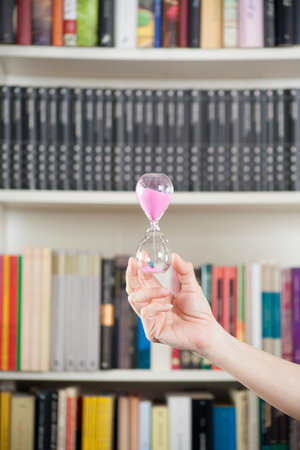 pink sand clock in woman hand over library background