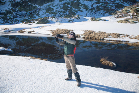 brunette woman with green, red and brown clothes with camera, as photographer taking selfie photo picture, in winter snow Gredos mountain, Avila, Spain, Europeの写真素材