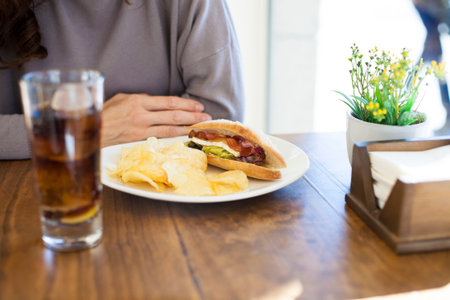hands of brunette woman mauve color sweater on light brown wooden table with bacon cheese lettuce...