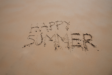 happy summer text written on brown sand ground at beachの写真素材