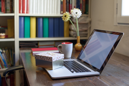 gift box with heart symbols on portable laptop on wooden table with cup of coffee and flowers at home. Nobodyの写真素材