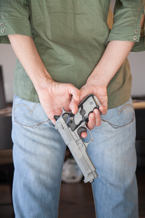 woman with blue jeans and green shirt with hands behind back with a plastic toy silver false pistol gunの写真素材