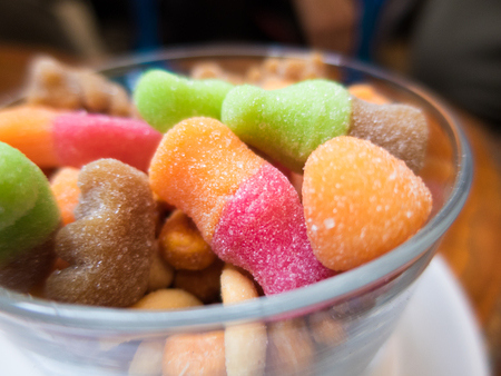 a lot of colorful candies assortment with shapes and sugar in a glass bowl. Orange, red, brown and greenの写真素材
