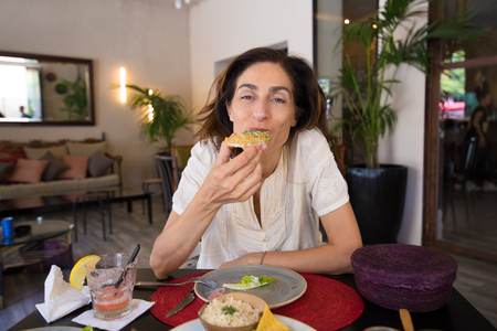 adult woman with white shirt looking and eating patties, sitting in black table with red mat straw of restaurant,の写真素材