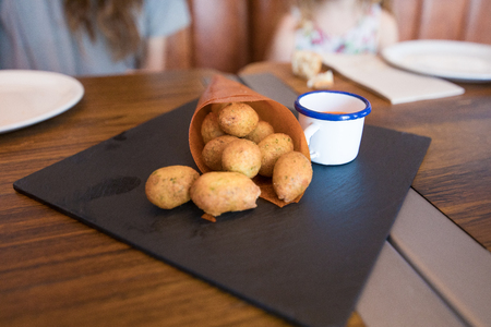 croquettes or cod fritters in paper cornet and sauce in white cup on black tray at restaurant, next to woman and childの写真素材